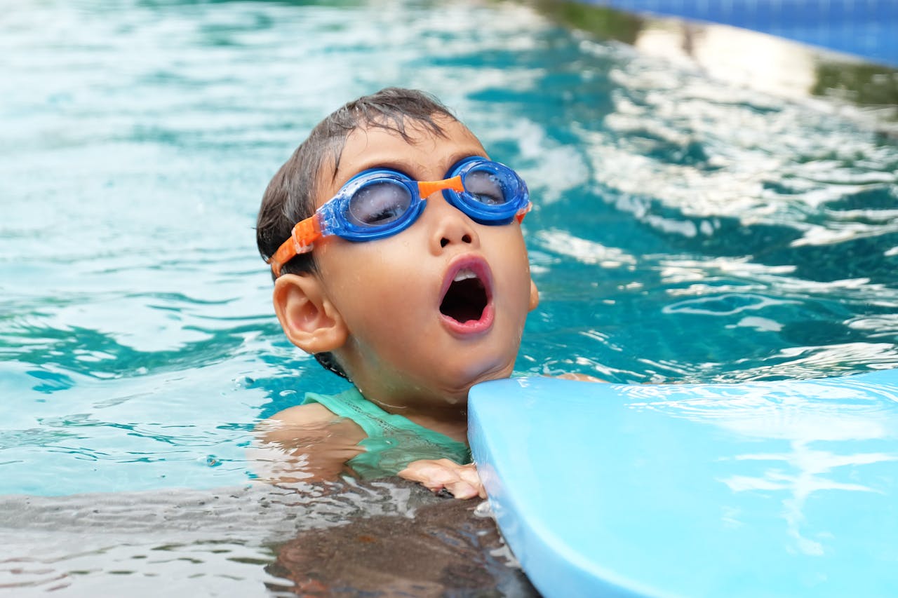 services-02 Young child swimming in a pool wearing blue goggles, enjoying summer.